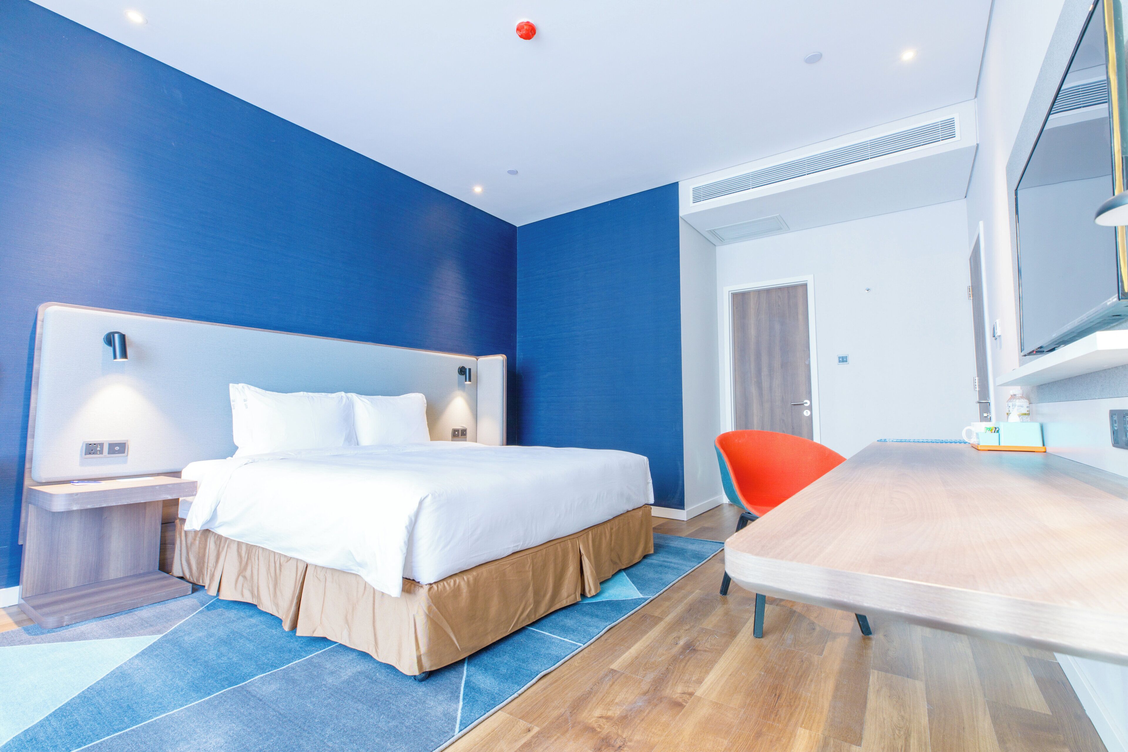 A modern hotel room with a large bed, a desk, and a chair.