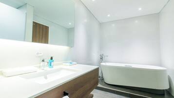 Un baño moderno con un espejo grande, un lavabo blanco, un mueble de tocador y una bañera independiente.