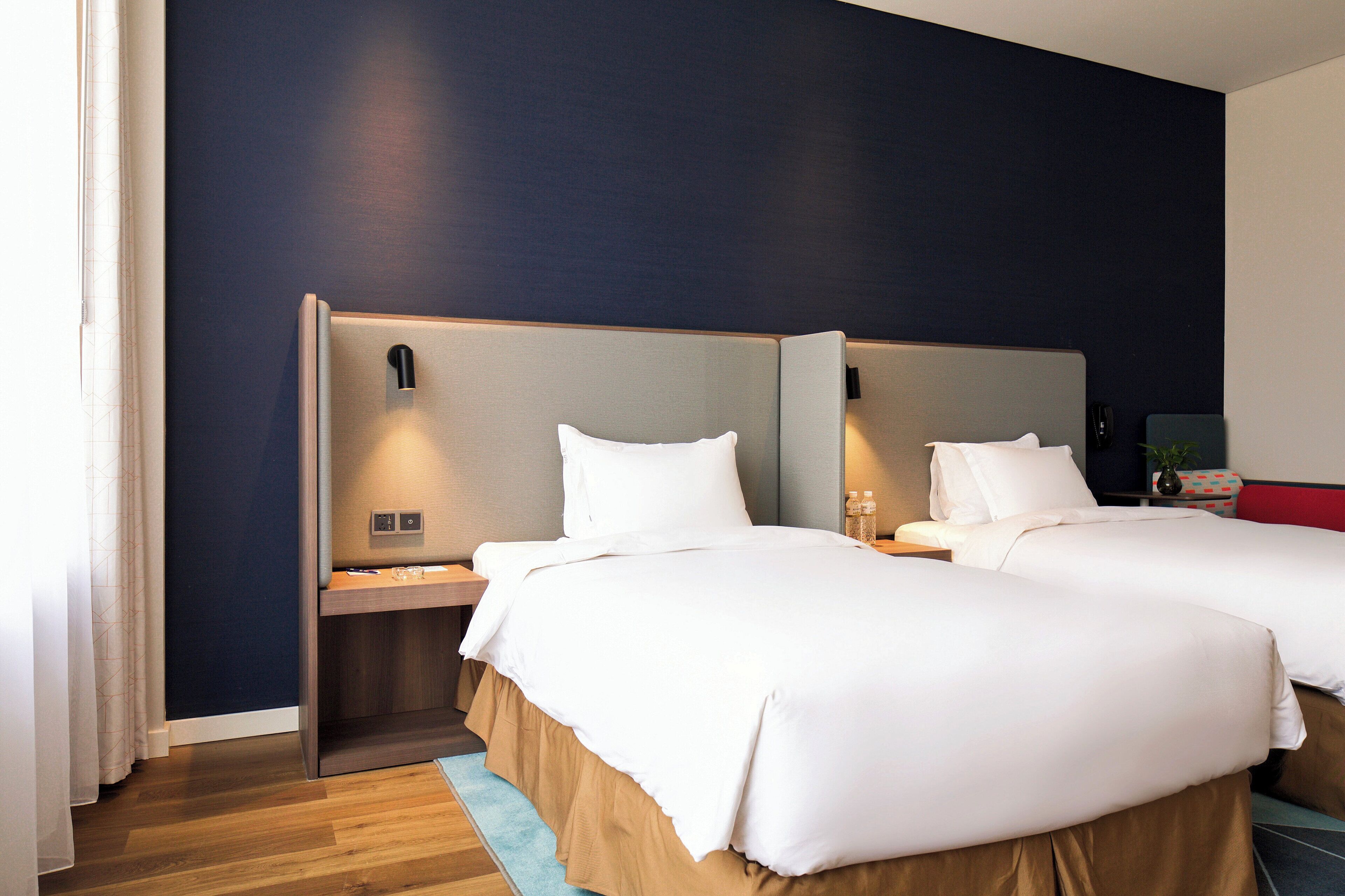 Habitación de hotel con dos camas, cabeceros de madera, una mesita de noche y una pequeña mesa con un florero.