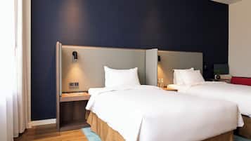 Habitación de hotel con dos camas, cabeceros de madera, una mesita de noche y una pequeña mesa con un florero.