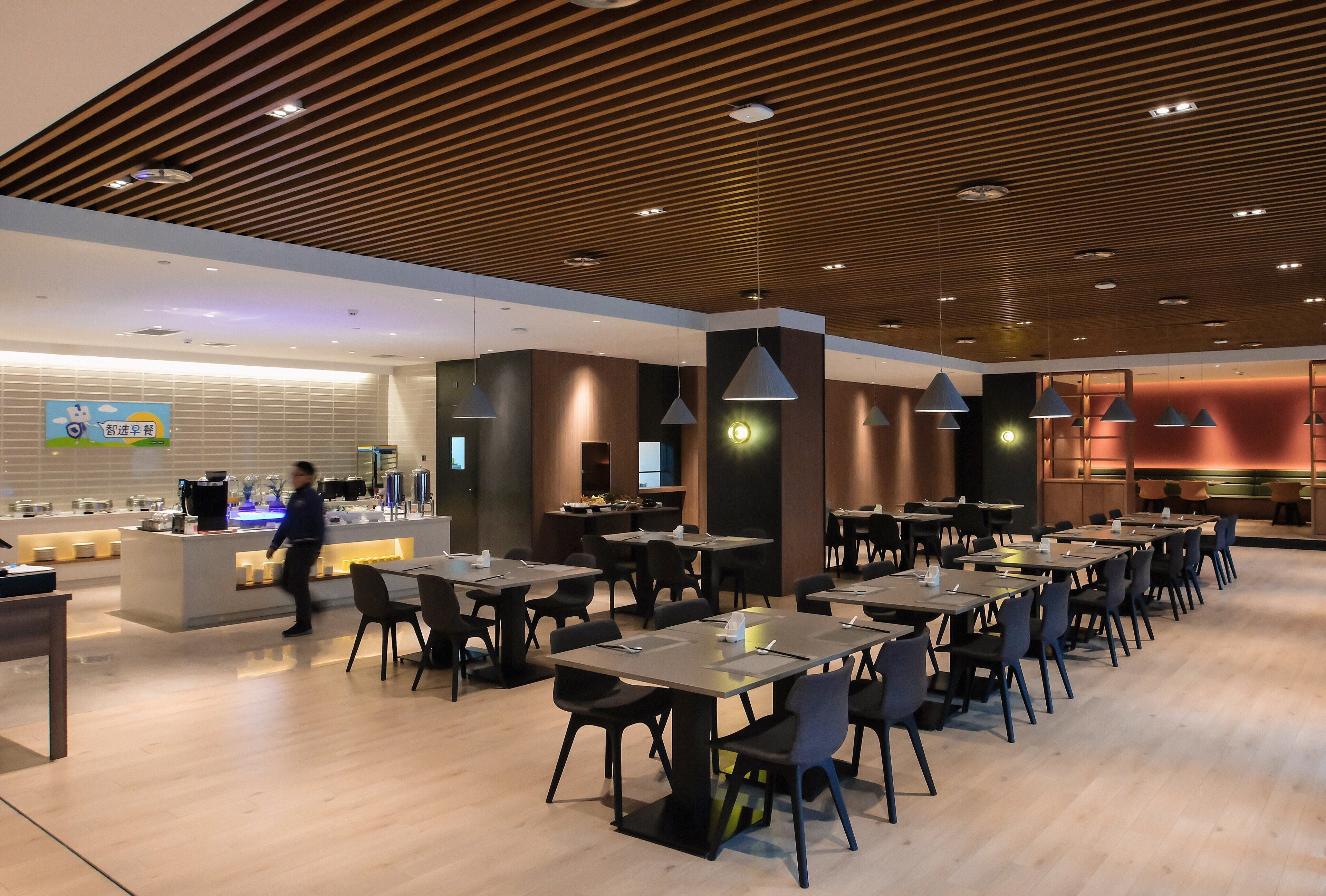 A modern restaurant with a wooden ceiling, multiple tables, and chairs.