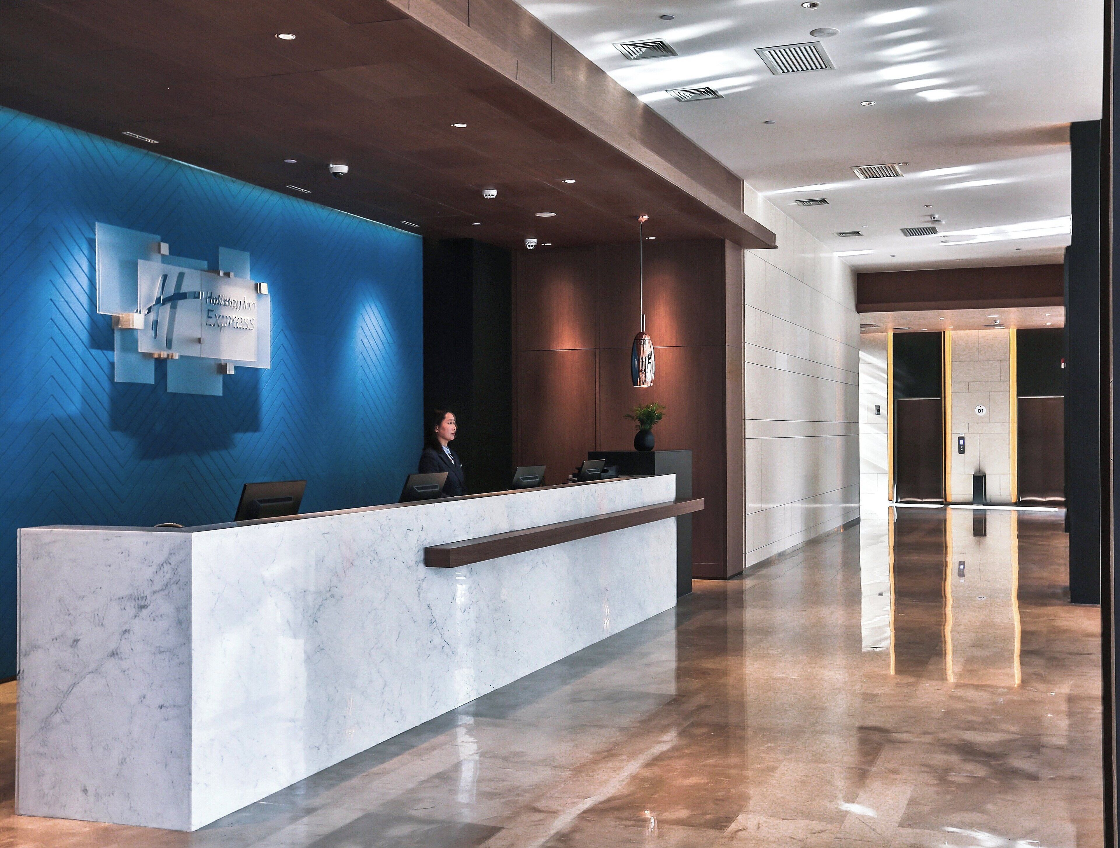Un mostrador de recepción de hotel con encimera de mármol, una recepcionista y una pared azul con diseño geométrico.