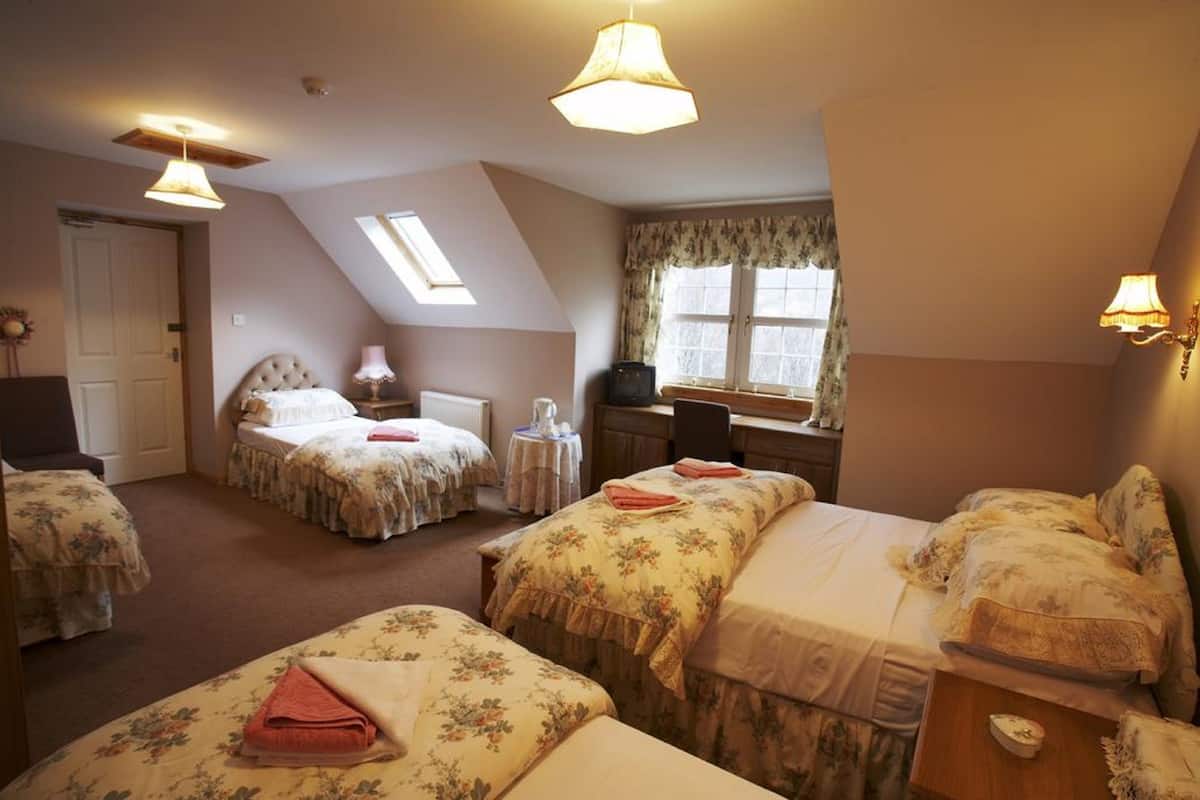 A bedroom with two beds, a desk, a chair, and a window with curtains.