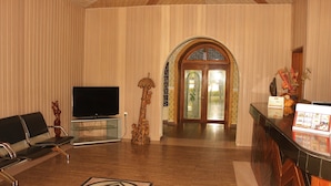 A hotel lobby with a TV, a reception desk, a wooden statue, and a patterned rug. - Jacaranda Suites (Calabar)