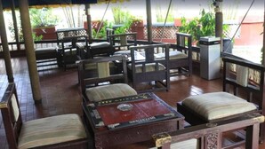 A covered outdoor seating area with wooden furniture and a table with a red top. - Jacaranda Suites (Calabar)