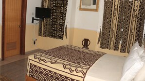Een hotelkamer met een bed, gordijnen, een televisie en een airconditioner.