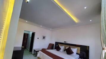 A hotel room with a bed, a chair, a small table, and a door leading to another room.