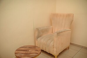 Habitación de esquina con un sillón de color claro y una pequeña mesa redonda.