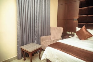 Quarto de hotel com cama, uma cadeira, uma mesa pequena e um guarda-roupa.