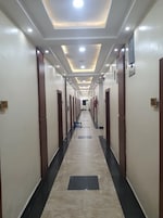 Corredor de hotel com piso de azulejos, portas em ambos os lados e iluminação embutida no teto.