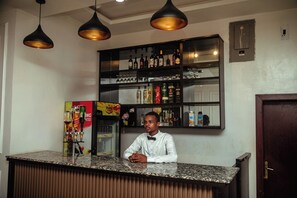 Una zona de bar con mostrador, estantes llenos de botellas y un refrigerador.