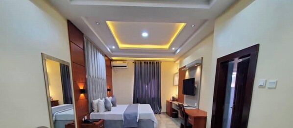 Habitación de hotel con cama, mesitas de noche, escritorio, televisor de pantalla plana y espejo.