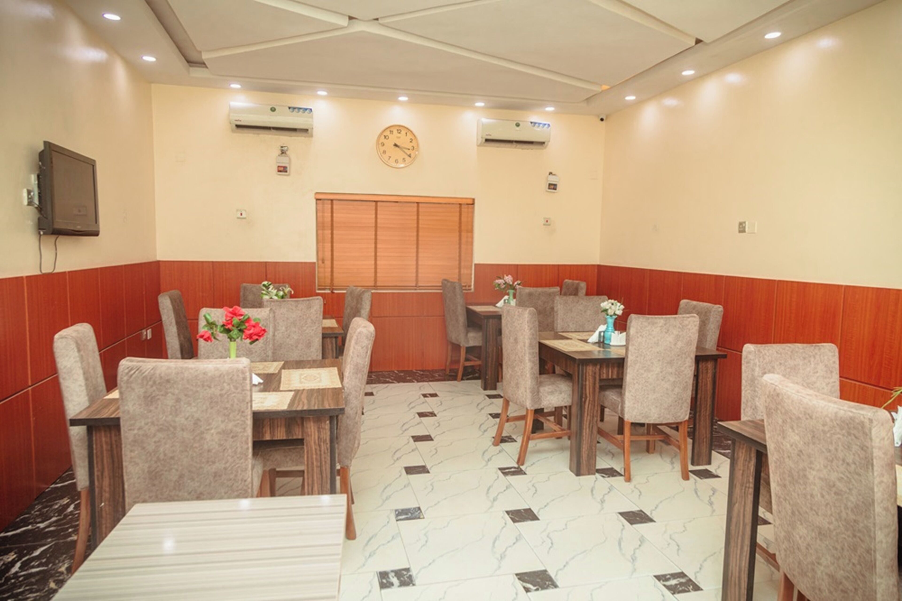 A hotel dining area with tables and chairs, a clock, and air conditioning units.