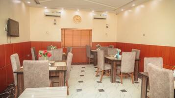 A hotel dining area with tables and chairs, a clock, and air conditioning units.