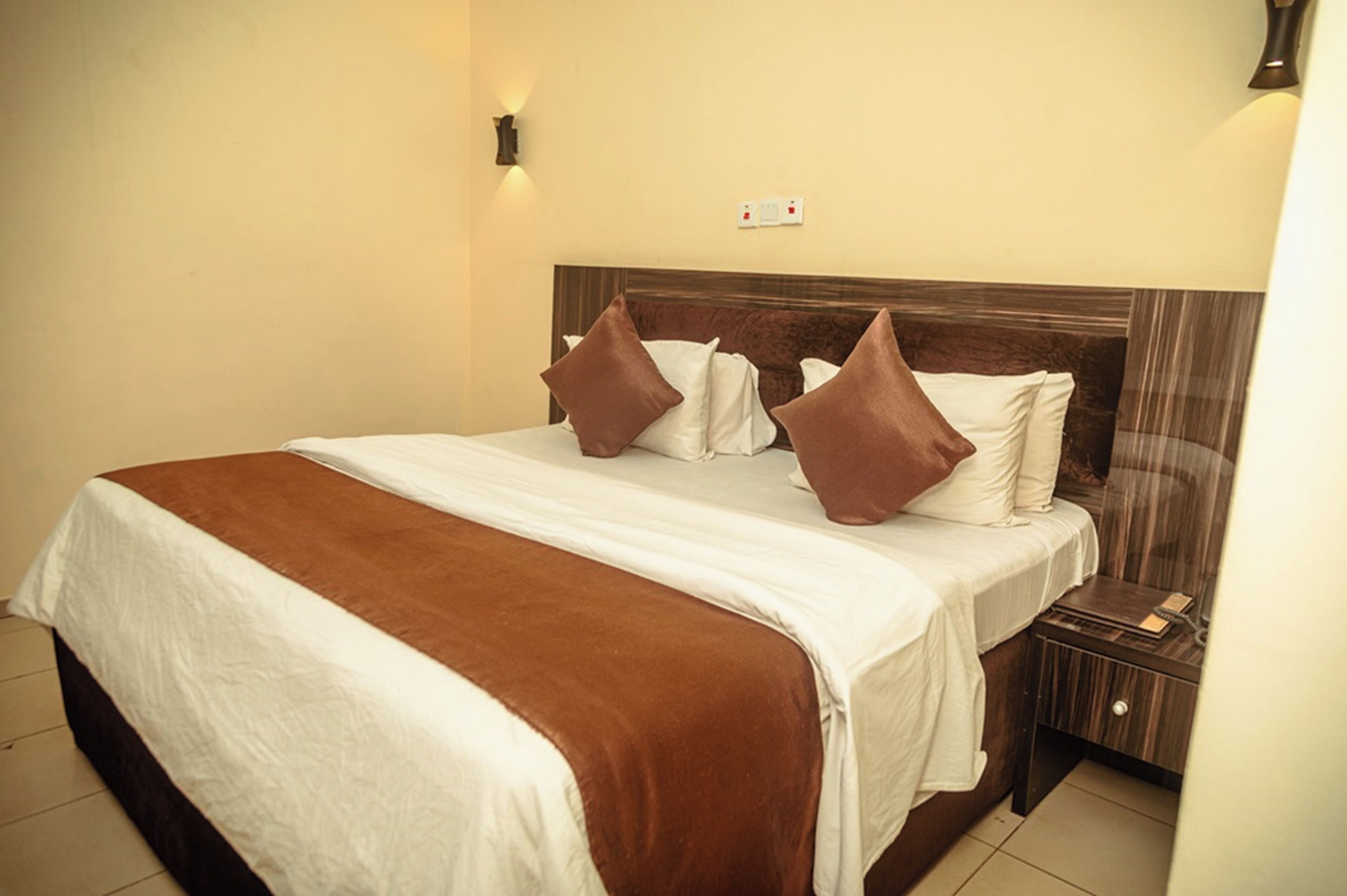 Habitación de hotel con cama, mesita de noche y lámpara fijada a la pared.