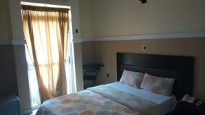 A bedroom with a bed, a chair, an air conditioning unit, and a window with curtains. - Modroy Hotel and Suites (Abeokuta)