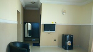 A room with a flat-screen TV mounted on the wall, a refrigerator, and a door leading to another room. - Modroy Hotel and Suites (Abeokuta)