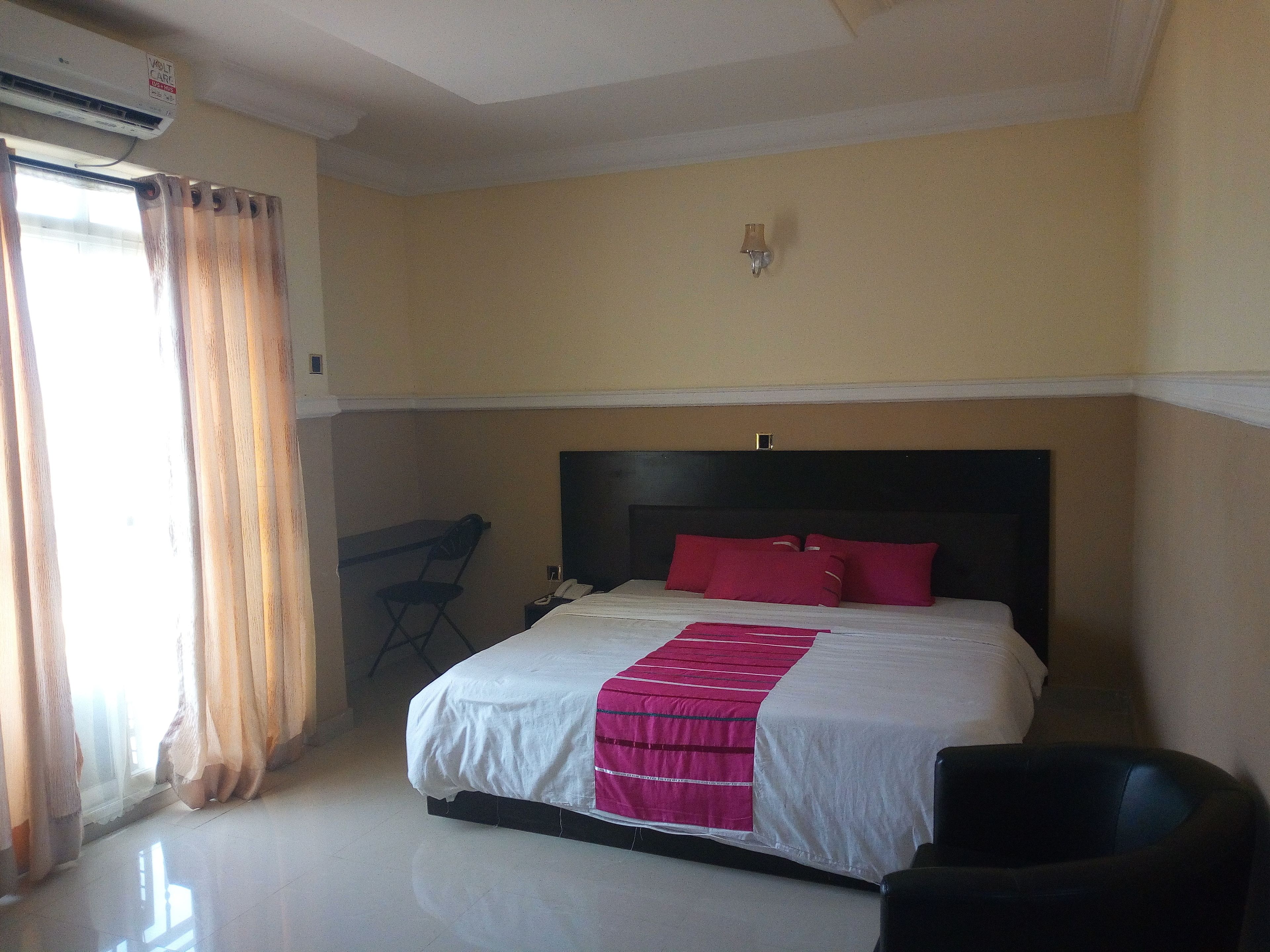 A hotel room with a bed, a chair, a desk, and an air conditioning unit.