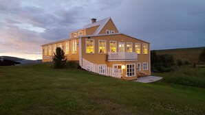 A two-story building with a balcony, a small porch, and a well-lit entrance. - Fosshóll Guesthouse (Laugar)