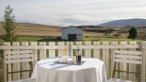 A table set outdoors with a view of a rural landscape, including a barn and hills. - Fosshóll Guesthouse (Laugar)