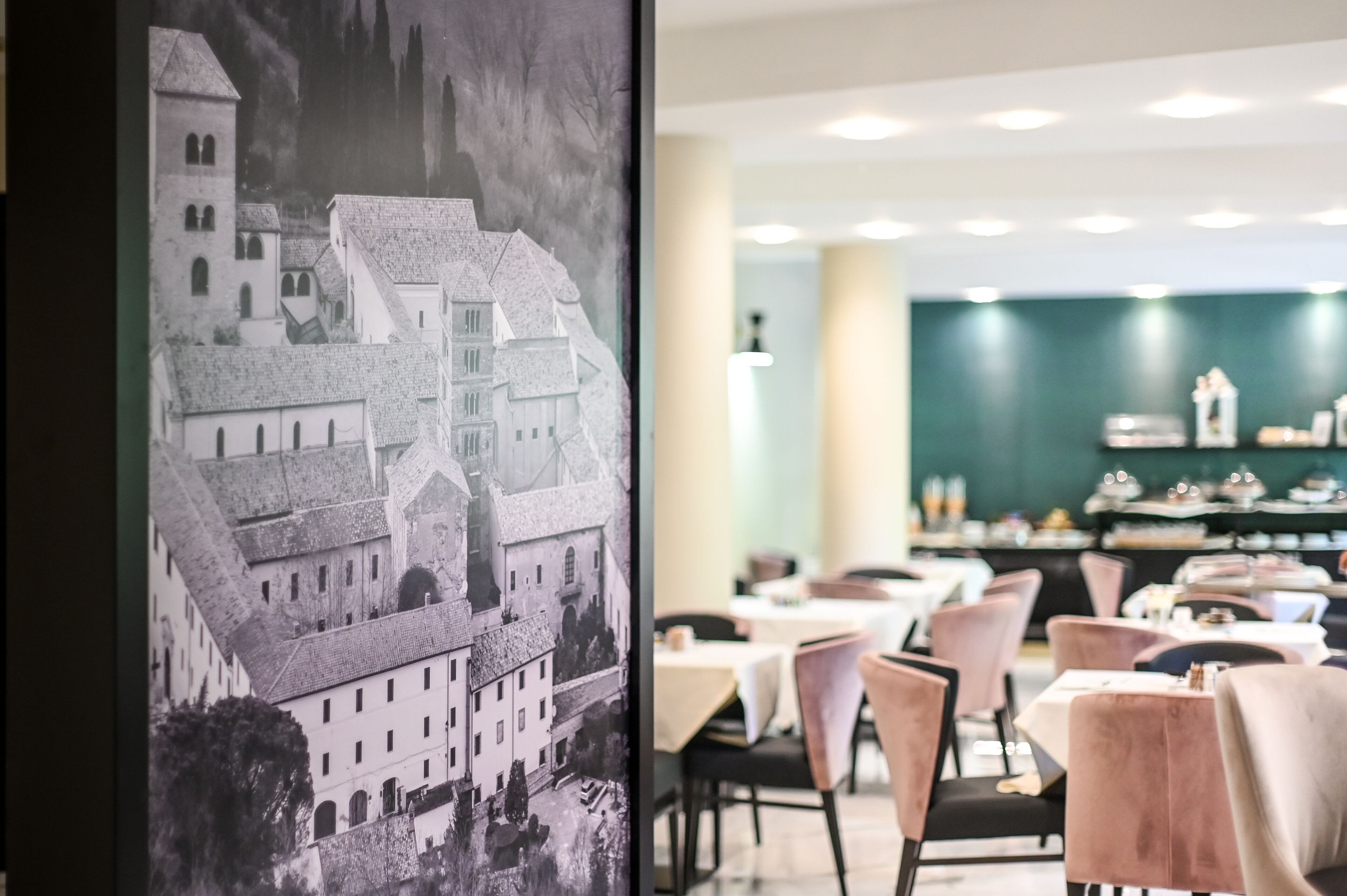 Interior de restaurante con mesas y sillas, un mural grande de un edificio histórico, y una pared verde con adornos.