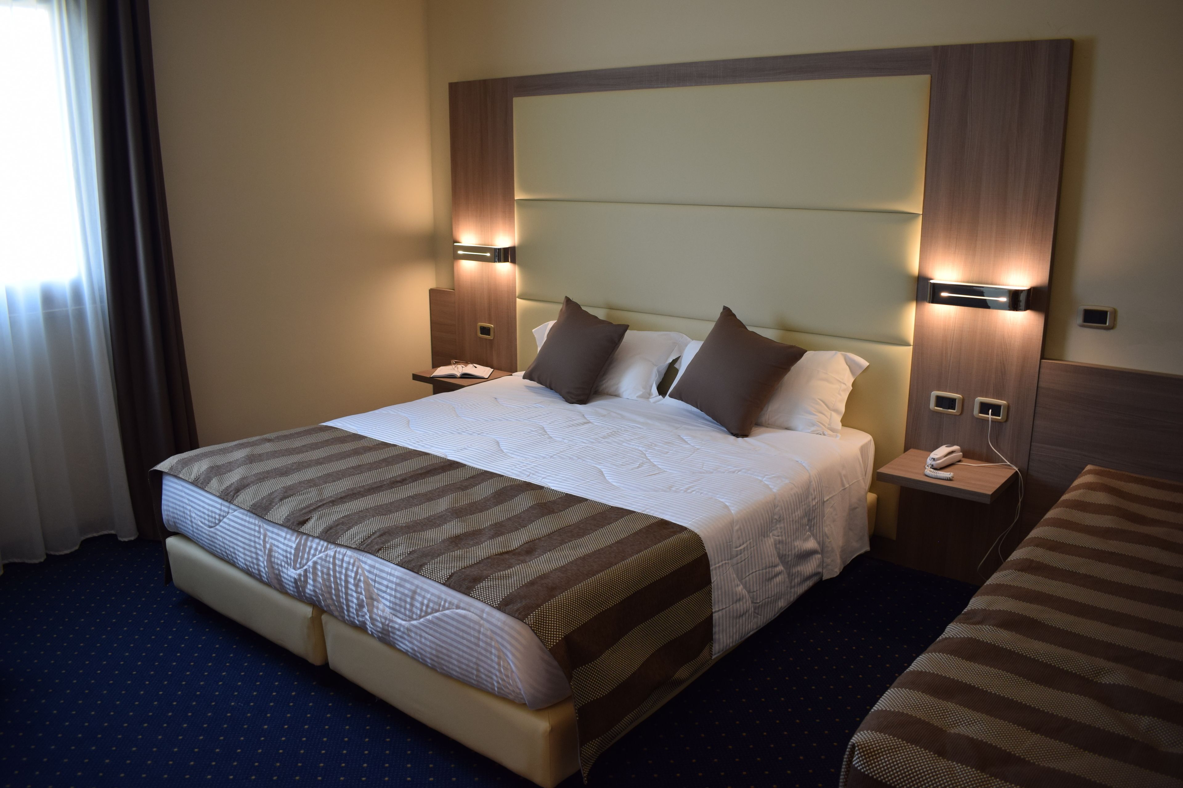 Une chambre d’hôtel avec un grand lit, une table de chevet avec un téléphone et une petite table de nuit avec une lampe.