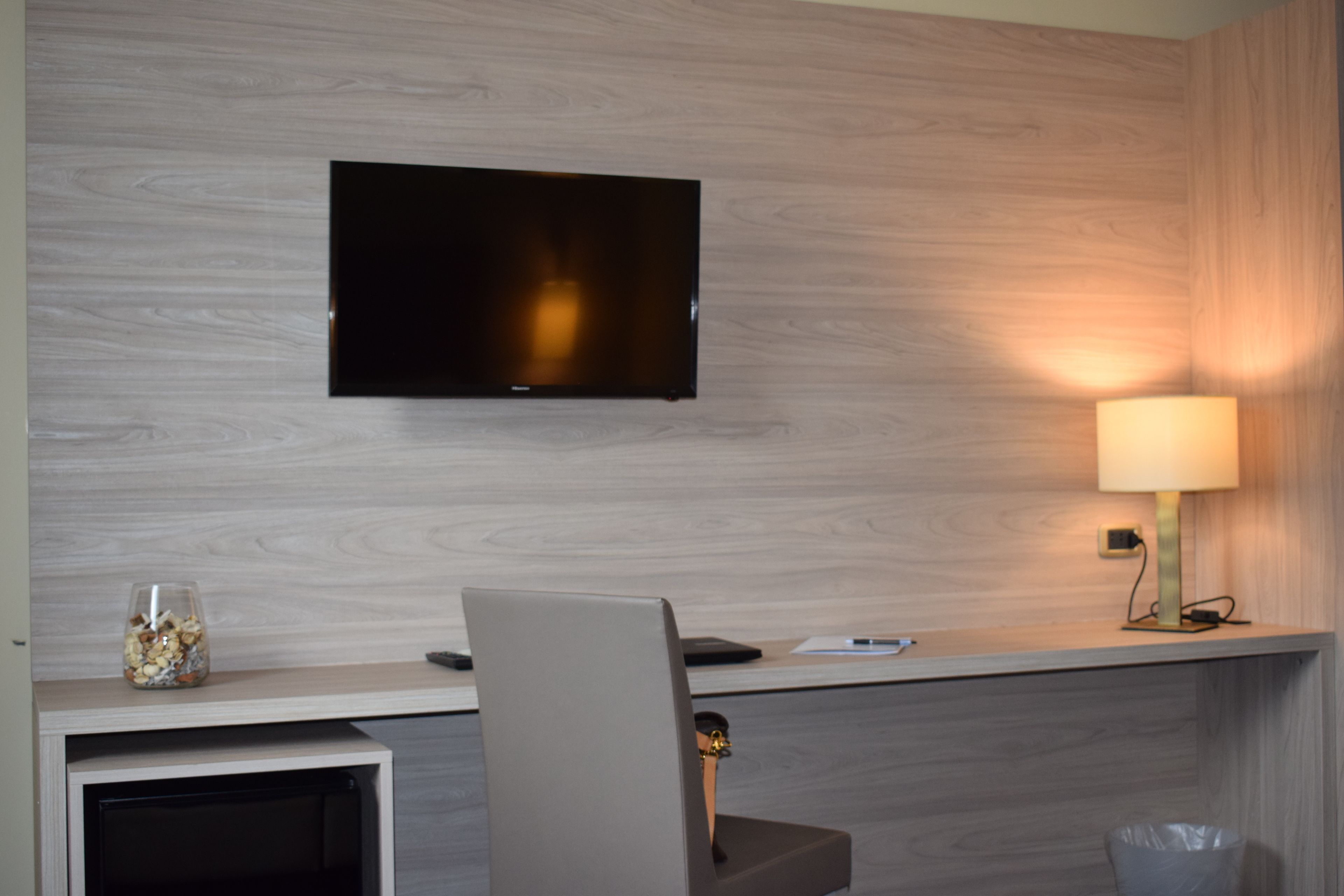 Una habitación moderna con un televisor de pantalla plana montado en una pared de madera, un escritorio con una lámpara y un cubo de basura.