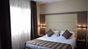 Una habitación de hotel con una cama grande, dos mesitas de noche y un ventanal con cortinas.