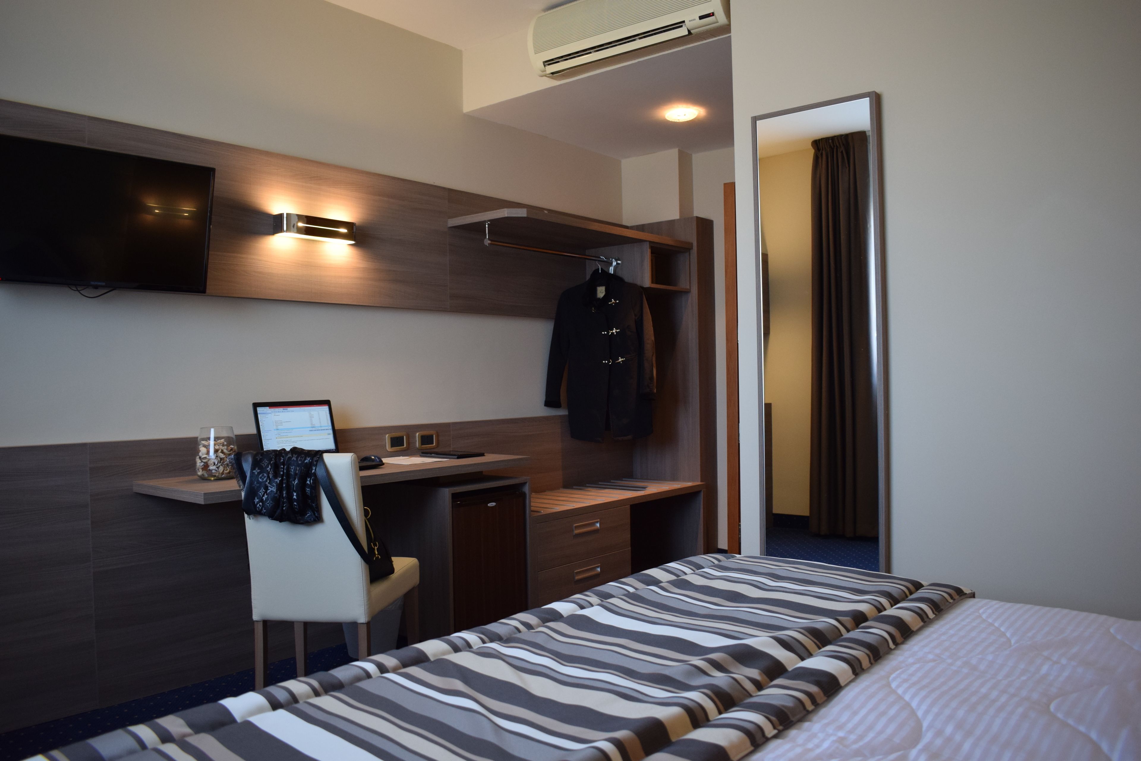 A modern hotel room with a bed, a desk, a chair, a TV, and a wardrobe.