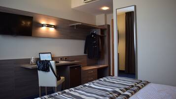 A modern hotel room with a bed, a desk, a chair, a TV, and a wardrobe.