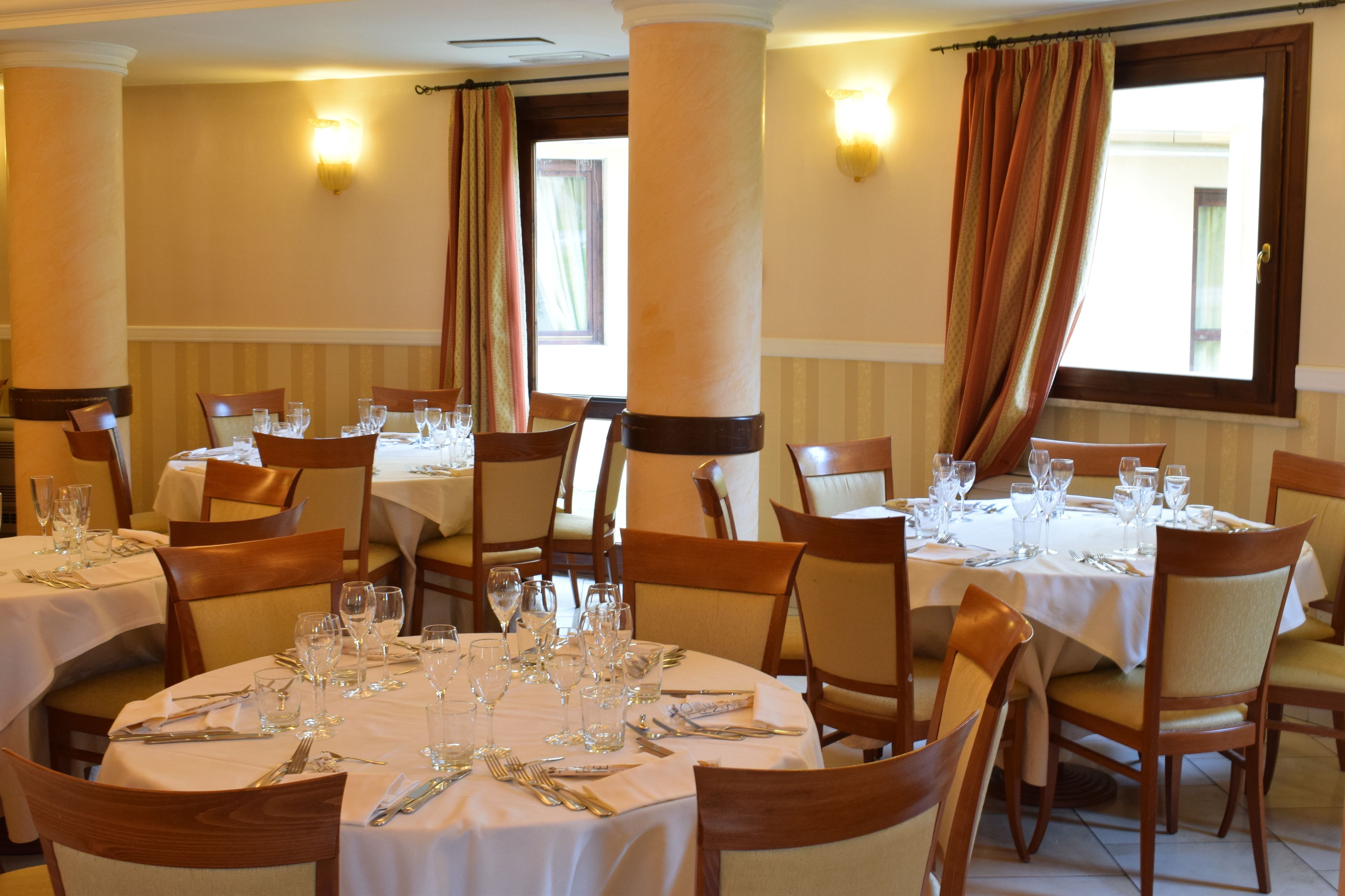 A dining area with round tables set for multiple guests, each table equipped with cutlery and glasses.