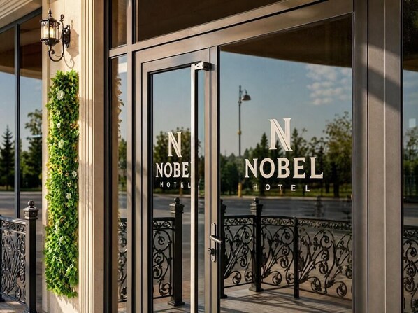 The entrance of the Nobel Hotel with a glass door and a metal gate.