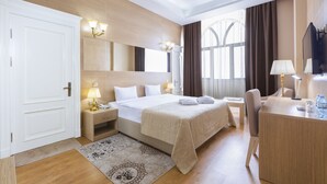 A hotel room with a large bed, bedside tables with lamps, a desk with a chair, a TV, and a window with curtains. - Nobel Hotel (Baku)