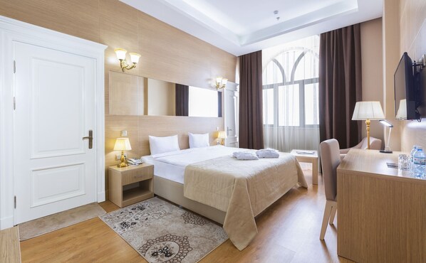 A hotel room with a large bed, bedside tables with lamps, a desk with a chair, a TV, and a window with curtains. - Nobel Hotel (Baku)