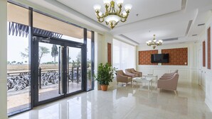 A spacious lobby with a large glass door leading outside, a chandelier, a television on the wall, and a seating area with chairs and a table. - Nobel Hotel (Baku)