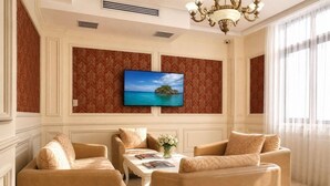 A living room with a flat-screen TV mounted on a wall, two sofas, a coffee table, and a chandelier. - Nobel Hotel (Baku)