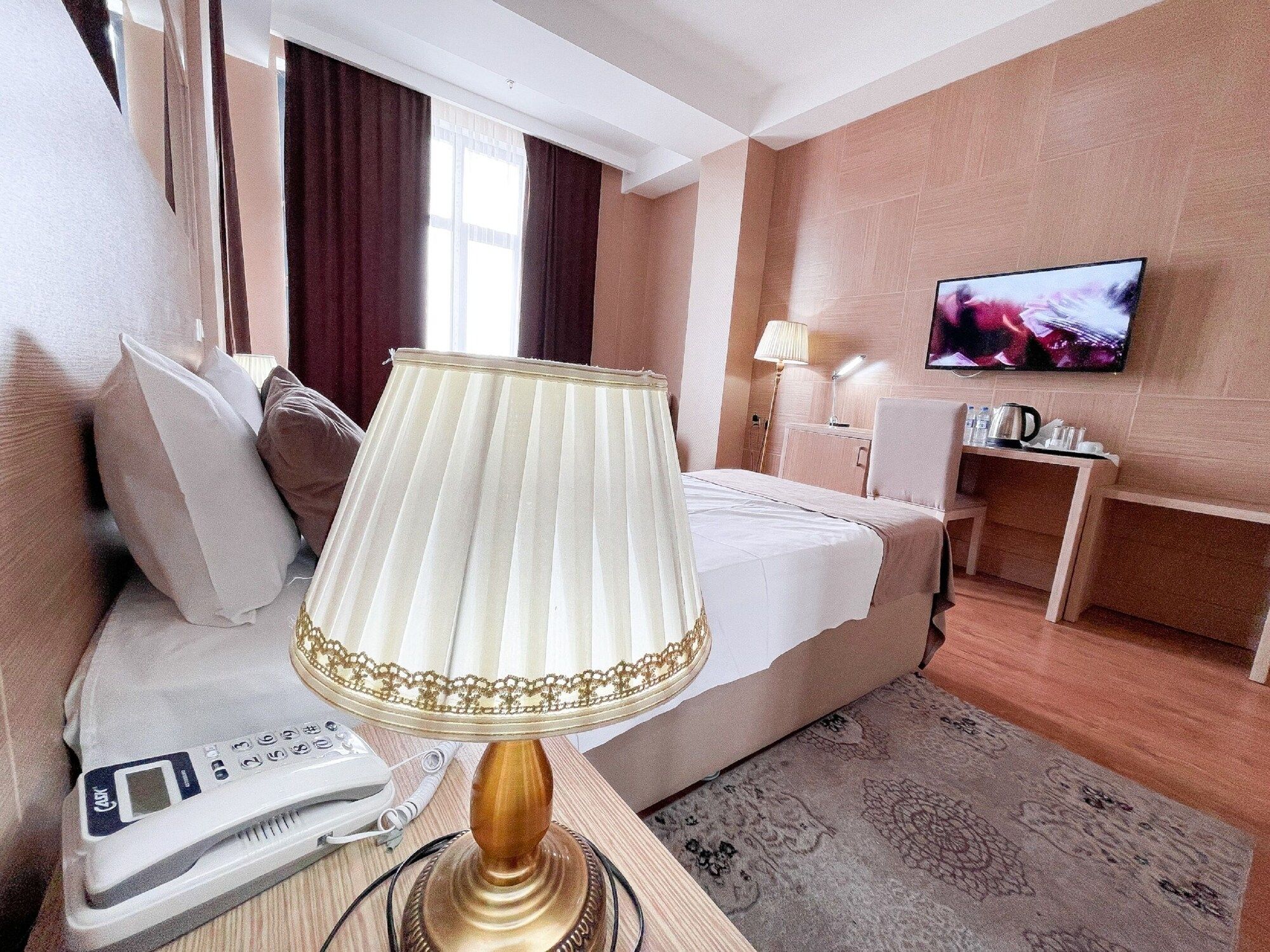 Quarto de hotel com cama, televisão, mesa de cabeceira com abajur, telefone e luminária decorativa.