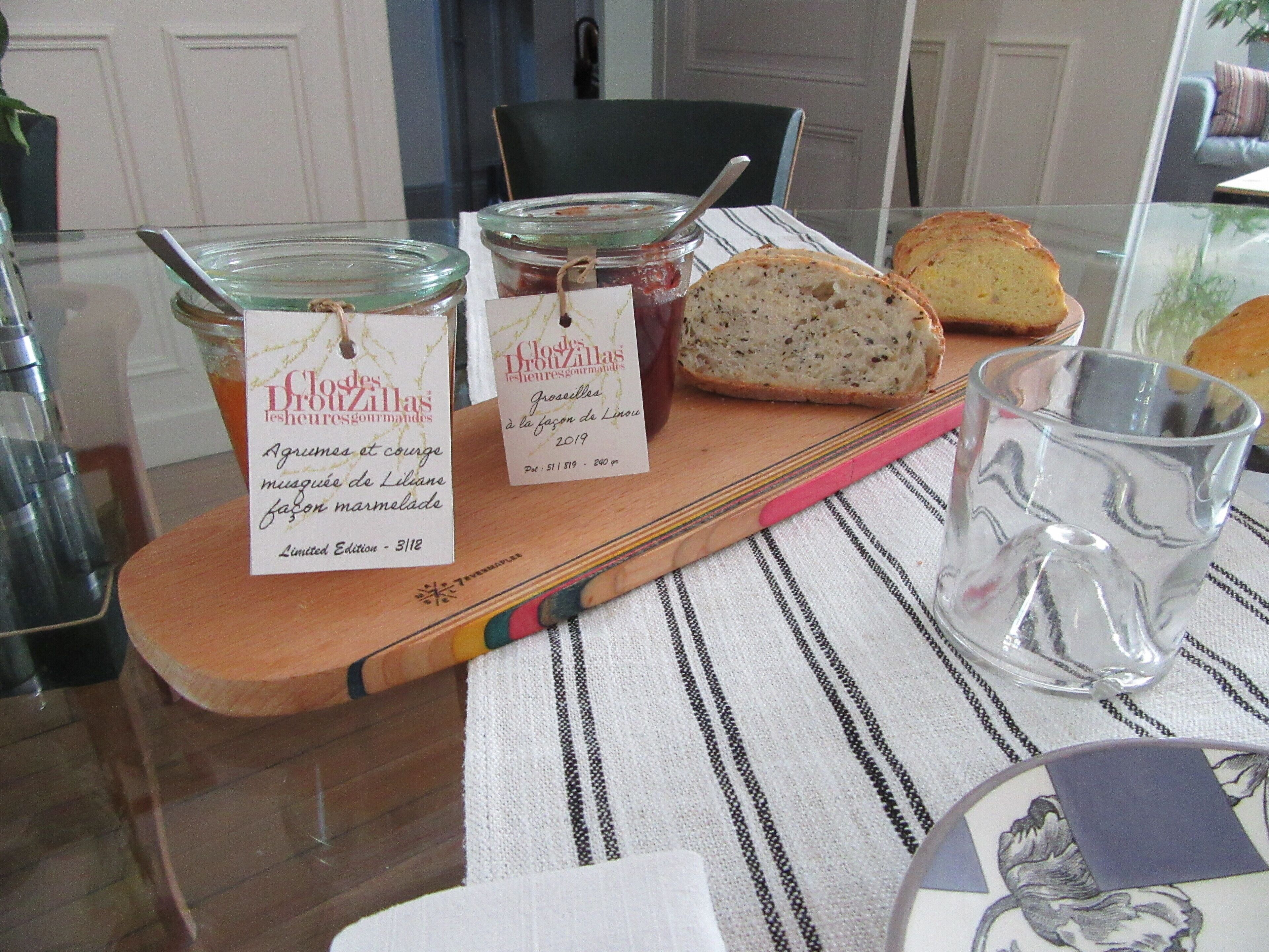 Un tagliere di legno con vasetti di conserve, pane, un bicchiere d'acqua e un sottobicchiere a righe.