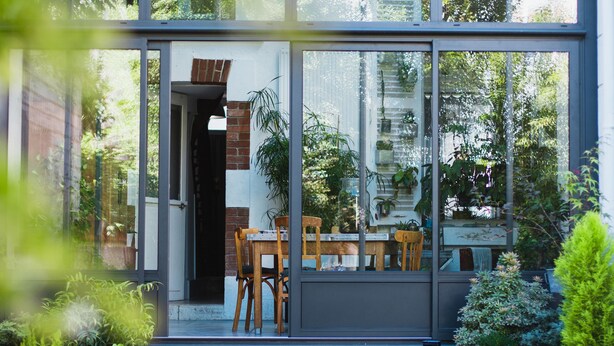 A modern house with a glass front, a wooden dining table, and chairs outside. - La Villa Dunois (Orléans)