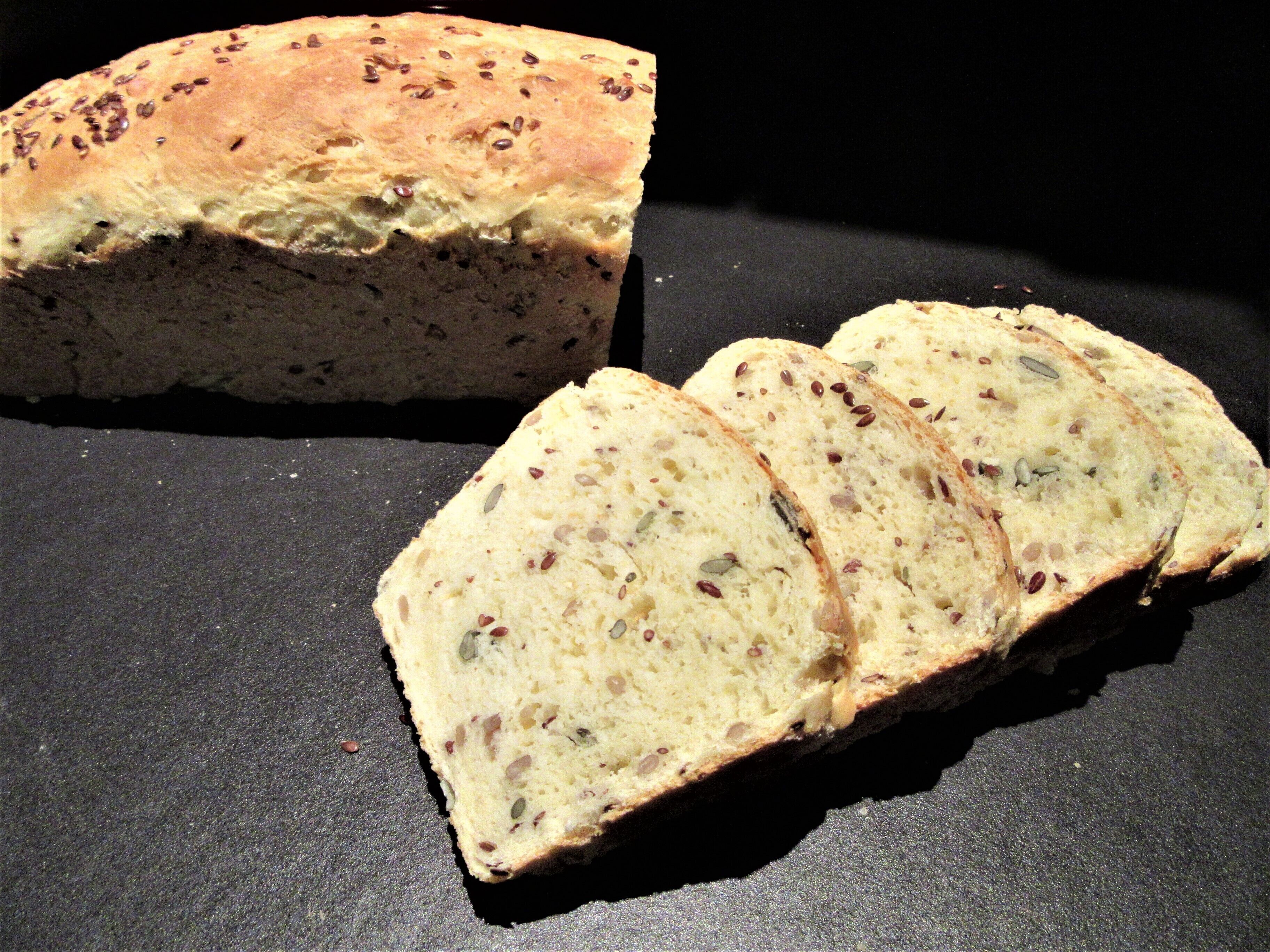 A loaf of bread with seeds on a dark surface.