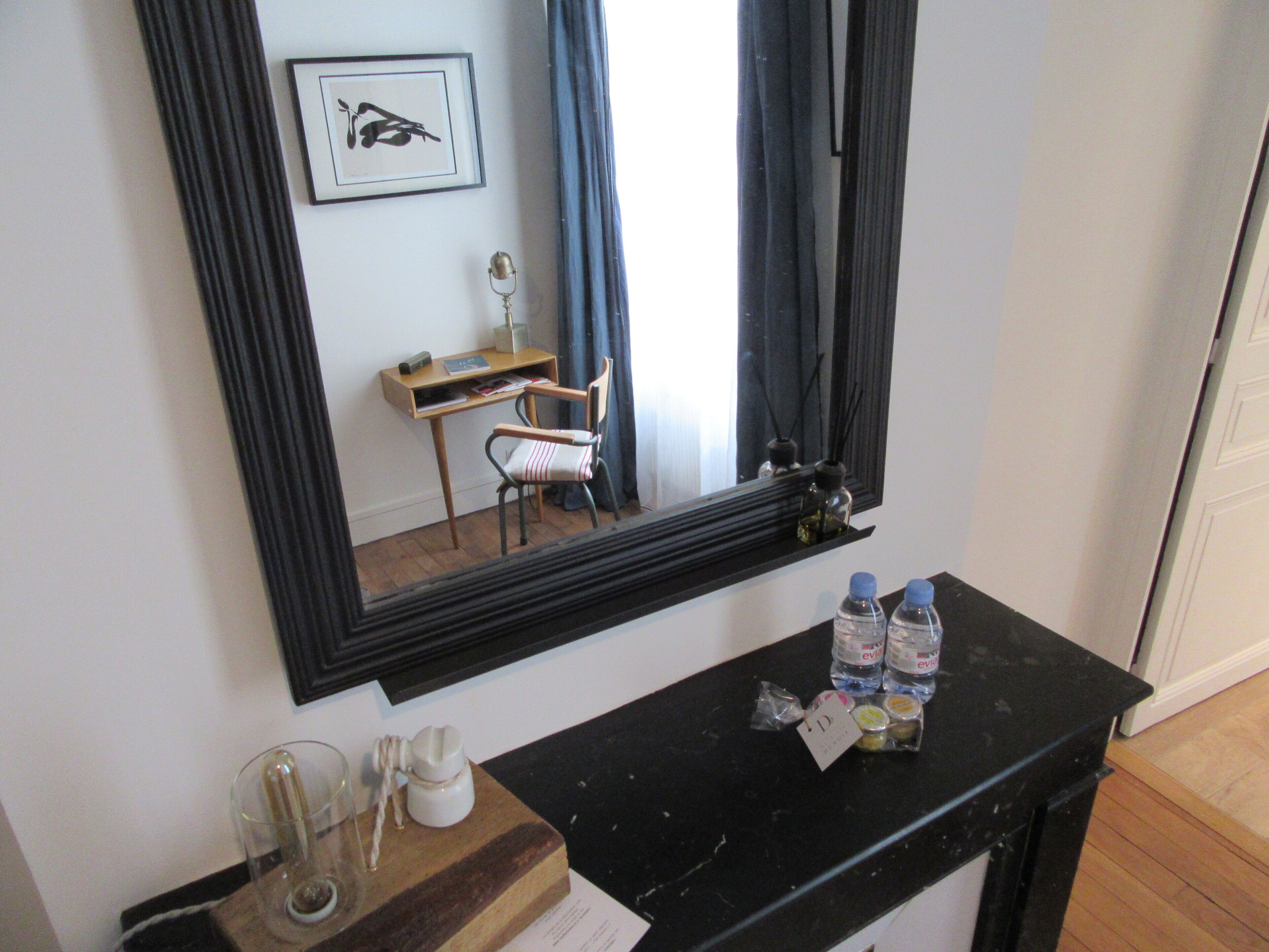 A room with a desk, chair, mirror, and a counter with bottles and a glass.