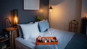 A neatly made bed with pillows, a bedside table with a lamp, a tray with breakfast items, and a framed abstract artwork on the wall. - La Villa Dunois (Orléans)