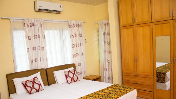 A bedroom with a bed, curtains, a wardrobe, and an air conditioning unit. - Jayliz Lodge (Accra)