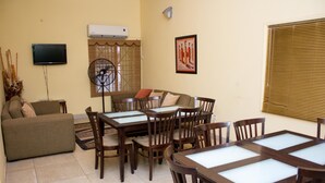 A living room with a sofa, a TV, a fan, and a dining area with chairs and a table. - Jayliz Lodge (Accra)