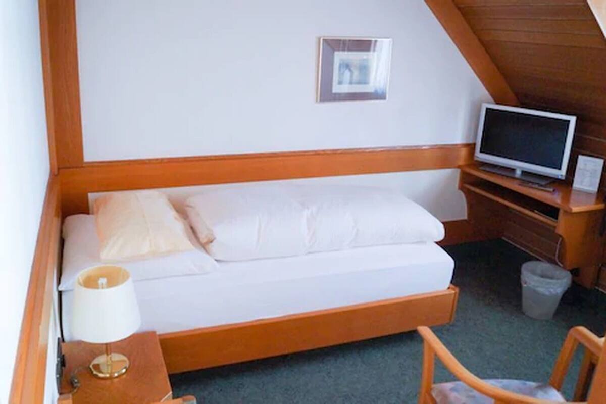 A small, cozy room with a single bed, a TV, a lamp, and a chair.