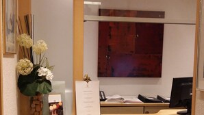 A reception desk with a wooden counter, a vase with flowers, a corkscrew container, and a menu on the wall. - Waldshuter Hof (Waldshut-Tiengen)