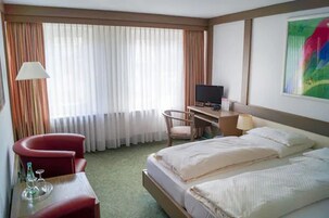 Quarto de hotel com cama, secretária com computador, cadeira e televisão.