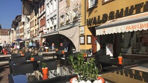 An outdoor café with tables and chairs, surrounded by buildings with shops and signs. - Waldshuter Hof (Waldshut-Tiengen)