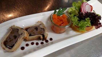 Ein weißer Teller mit aufgeschnittenem Fleischlabkuchen, einem kleinen Glas Karowürfeln und einem gemischten Blattsalat mit Radieschen.