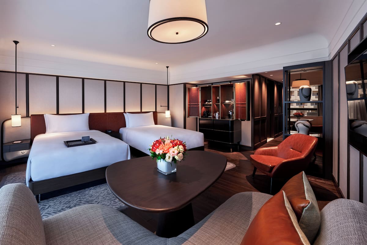 Een hotelkamer met twee bedden, een bijzettafeltje met bloemen, een bank, een rode fauteuil en een televisie.